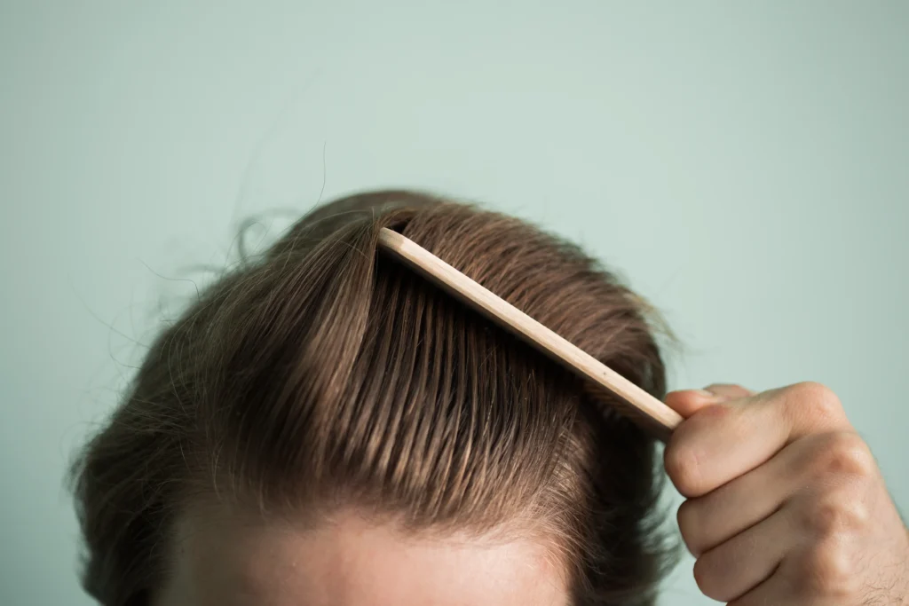 Person using a comb to part hair and examine the scalp