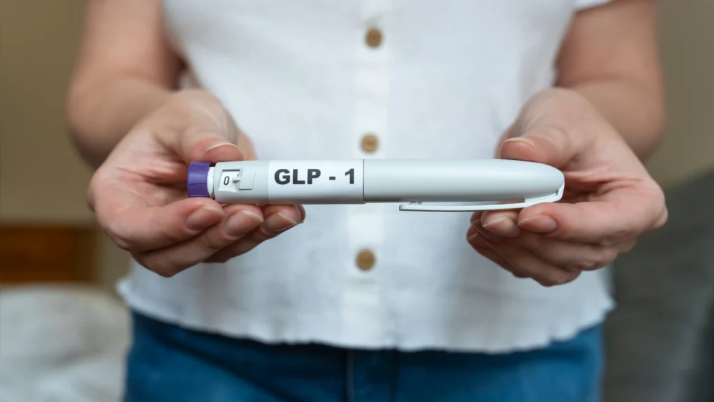 Person holding a GLP-1 injection pen with both hands against a blurred indoor background