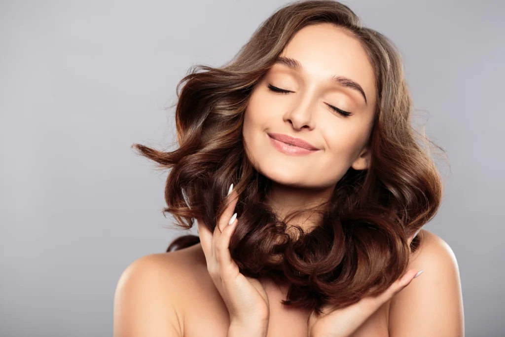 Person with eyes closed touching smooth, styled hair against a gray background
