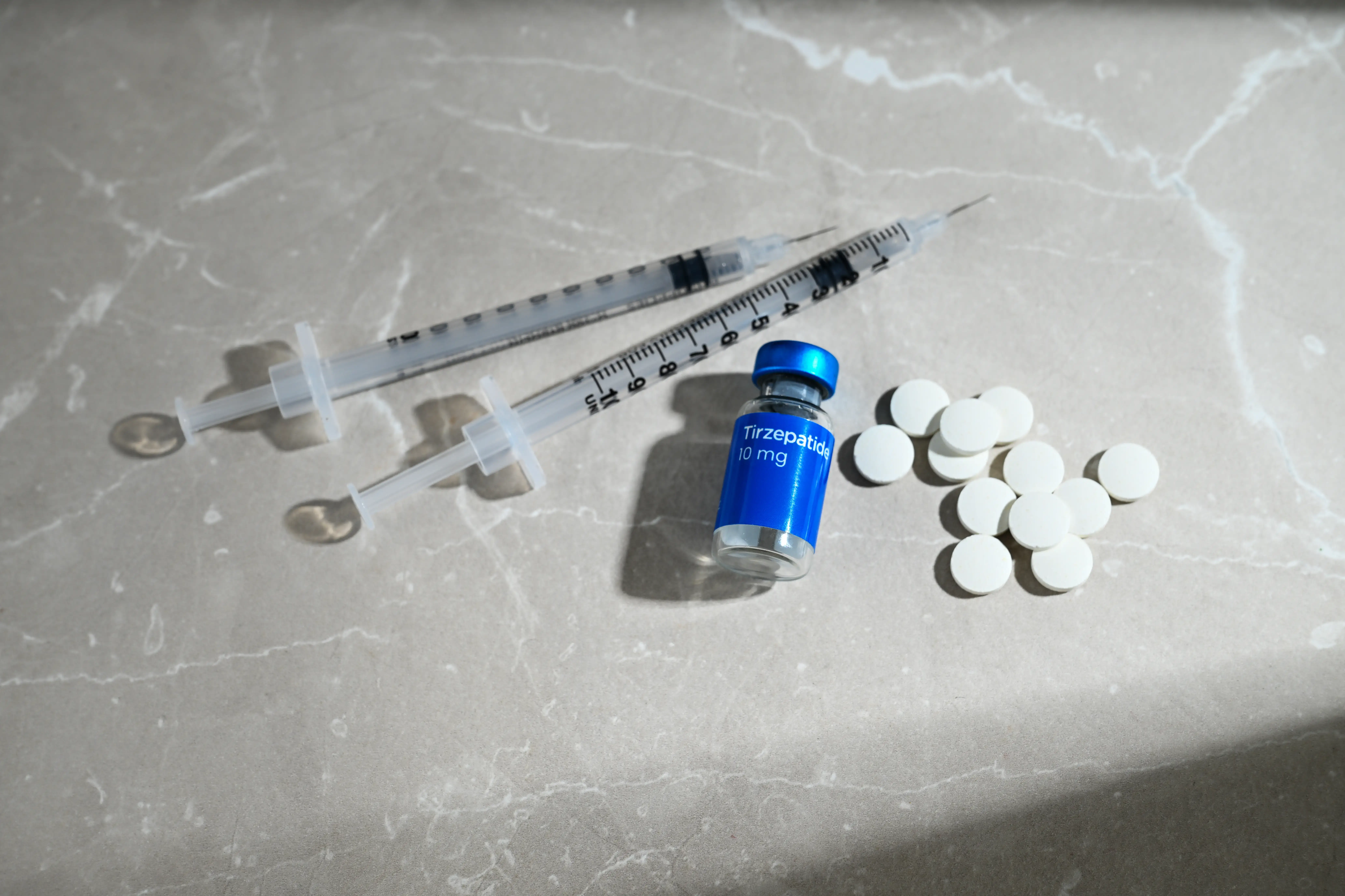 Medication vial, syringes, and white tablets arranged on a stone surface