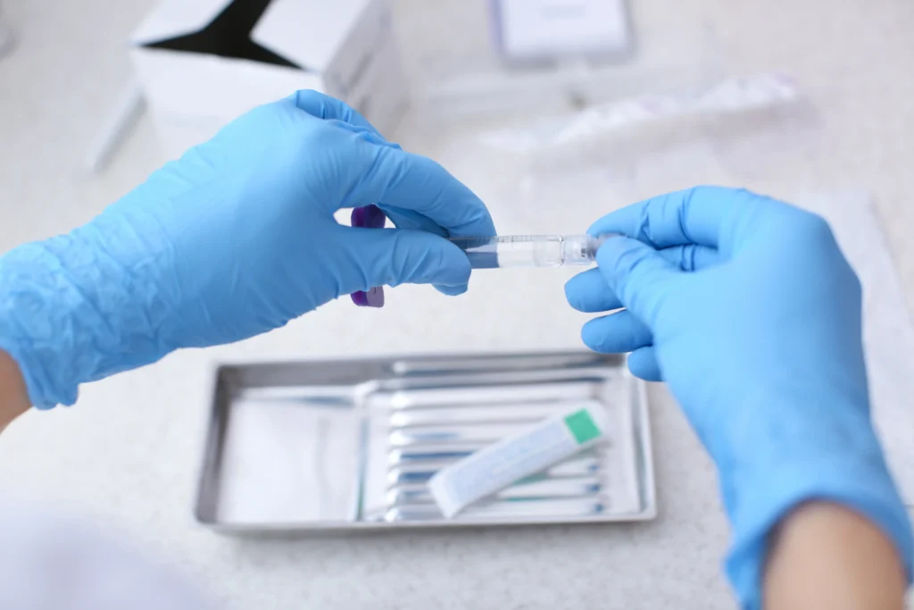 Gloved hands preparing a syringe on a medical tray with clinical supplies in the background