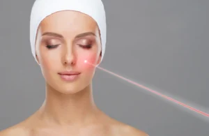 Woman with closed eyes has a red light directed toward one cheek against a gray background